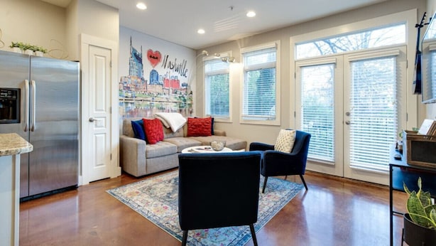 Una cocina moderna con un refrigerador de acero inoxidable, un comedor con sofá y sillas, y un mural de Nashville en la pared.