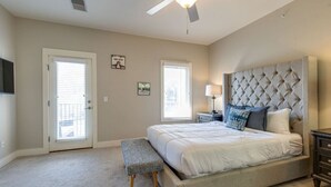 A bedroom with a large bed, a ceiling fan, a bench, and two windows.