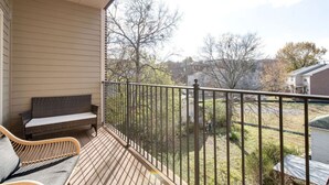 A balcony with a wooden floor, a wicker sofa, and a metal railing.