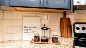 Een keuken met donkerblauwe kastjes, een koffiezetapparaat en een bord met een citaat.