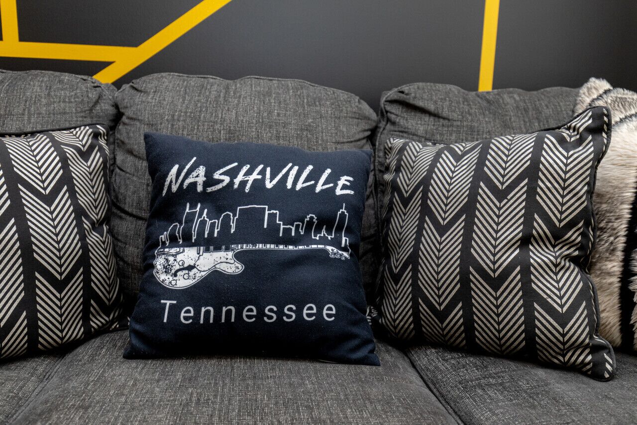 A gray sofa with three decorative pillows, one featuring a city skyline and the word "Nashville" and "Tennessee."