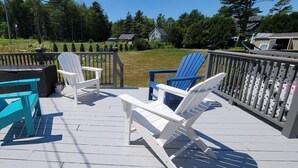Une terrasse avec coin salon extérieur comprenant deux chaises Adirondack turquoise et deux chaises Adirondack blanches, une petite table et un barbecue.