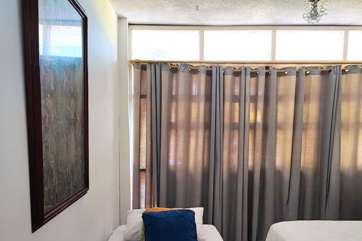 Ein Hotelzimmer mit Bett, Kissen, einem Fenster mit Vorhängen und einem Gemälde an der Wand.