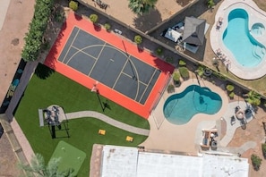 An aerial view of a property with a basketball court, a swimming pool, and a patio area.