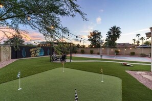 A backyard with a putting green, a patio area, and a mural on the wall.