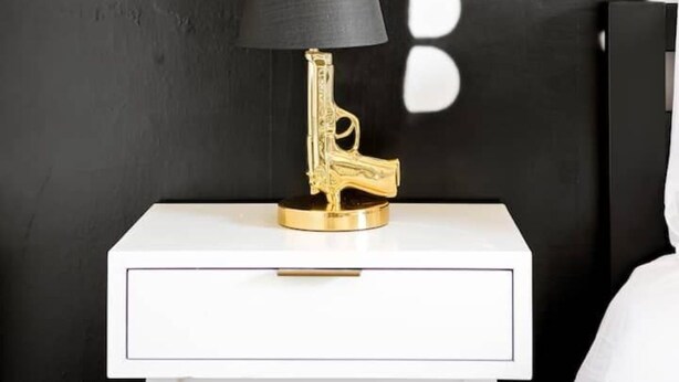 A white bedside table with a gold lamp featuring a black shade and a gold base.