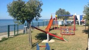 A playground with a seesaw, a slide, and a swing set near a body of water. - Apartments Topić - One Bedroom Apartment with Terrace (First Floor) (Privlaka)