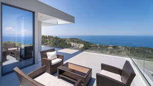 A modern balcony with wicker furniture, glass doors, and a scenic ocean view. - zenvillas.gr (Lefkada)