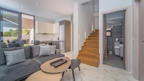A modern living room with a grey sofa, a round table, and a staircase leading to a kitchen. - zenvillas.gr (Lefkada)