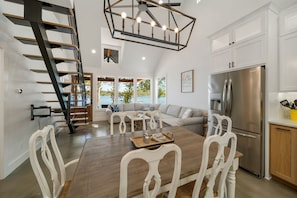 A spacious kitchen with a stainless steel refrigerator, a dining area with a wooden table and white chairs, and a staircase with a modern design. - Grand Lake Waterfront (Eucha)