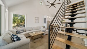 Un salon moderne avec un grand canapé d’angle gris, une table basse en bois et un escalier doté d’une rampe noire.