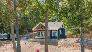 Une petite cabane dotée d’un porche et de meubles d’extérieur, entourée d’arbres et bordée d’un sentier de terre.