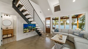 Un salon spacieux doté d’un escalier moderne, d’un grand tableau, d’un ensemble de canapés et offrant une vue sur l’extérieur.