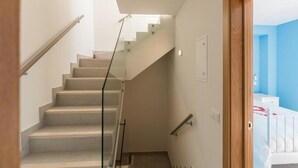 A staircase with glass railings leading to a room with a blue wall and a white bed. - Seaview Townhouse by the riverside in the centre of Alvor (with terrace) (Alvor)