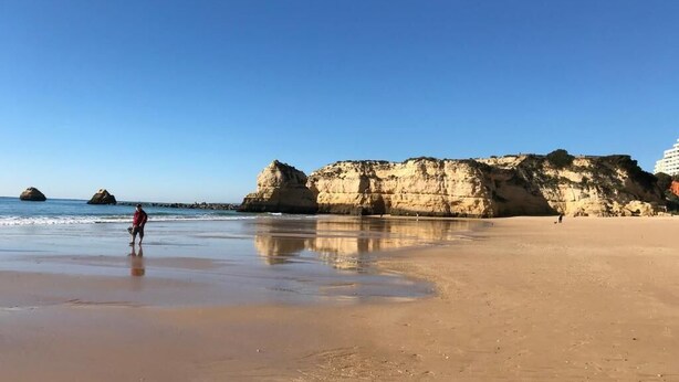 A beach with clear skies, a person walking, and rocky cliffs in the background. - Seaview Townhouse by the riverside in the centre of Alvor (with terrace) (Alvor)
