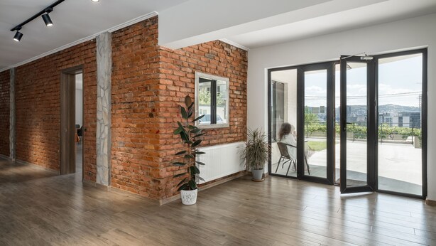A spacious room with a brick wall, a large sliding glass door leading to an outdoor area, and a potted plant. - Basa Boutique Hotel (Tbilisi)