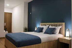 A modern bedroom with a large bed, wooden headboard, bedside lamps, and a potted plant. - Basa Boutique Hotel (Tbilisi)