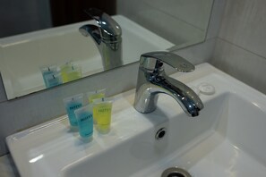 A hotel bathroom sink with a chrome faucet and a mirror above it. There are three toiletries on the sink: a blue bottle, a yellow bottle, and a green bottle. - Basa Boutique Hotel (Tbilisi)
