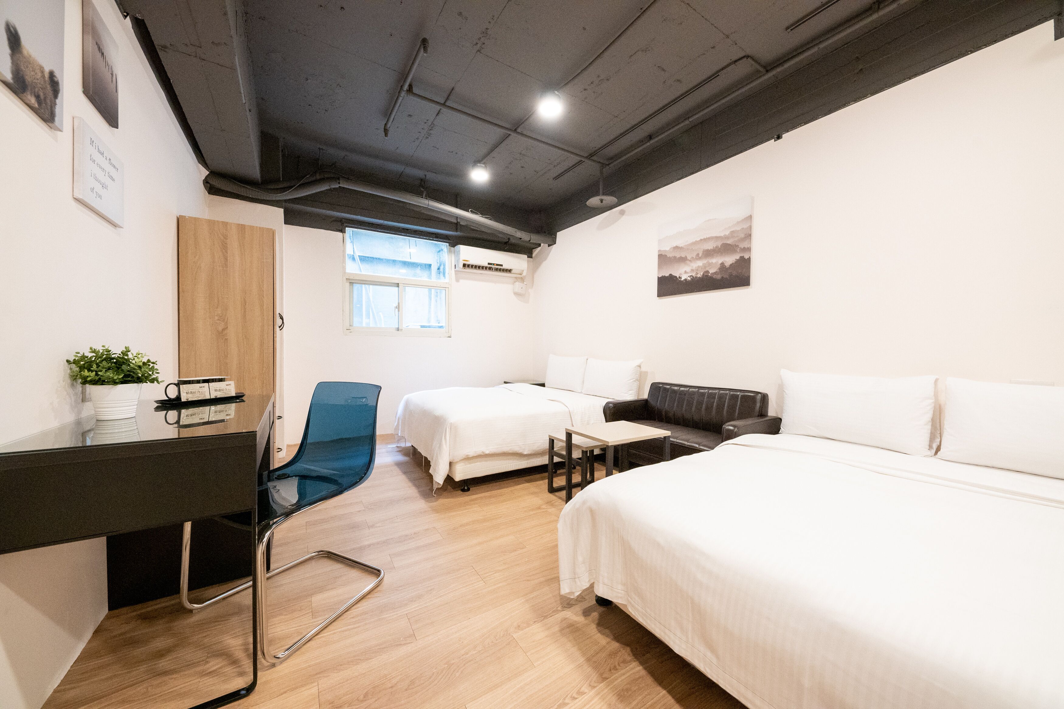 A modern hotel room with a wooden desk, two single beds, a sofa, and a blue chair.