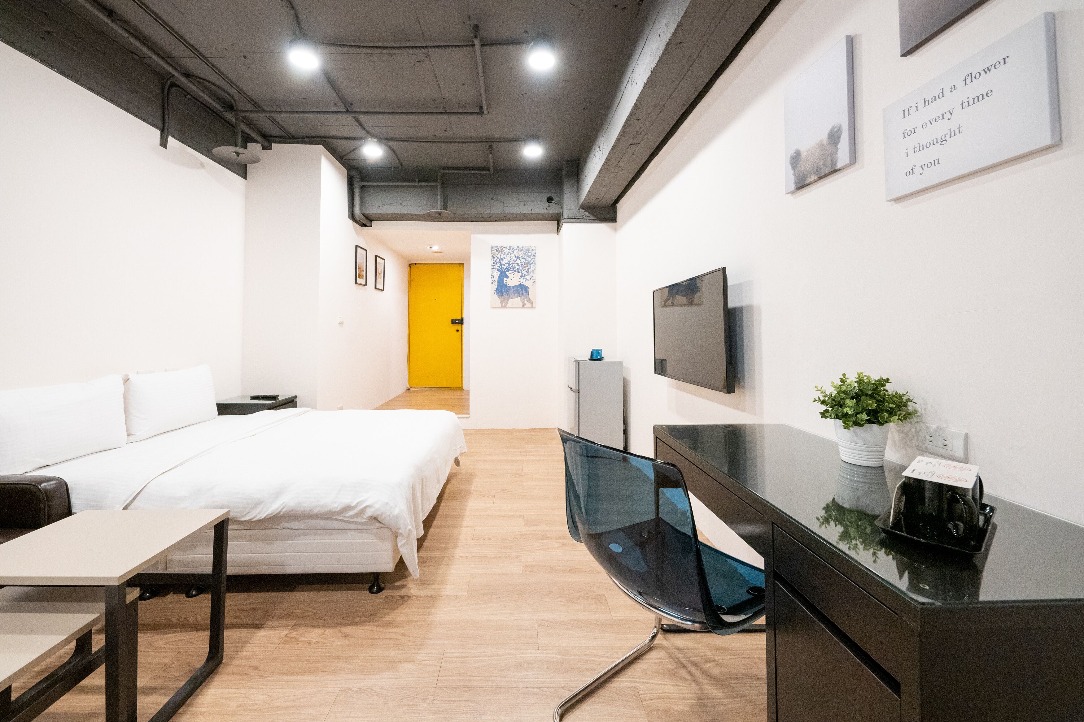 A modern hotel room with a bed, desk, and a TV on the wall.