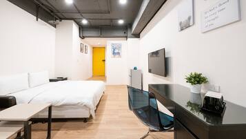 A modern hotel room with a bed, desk, and a TV on the wall.