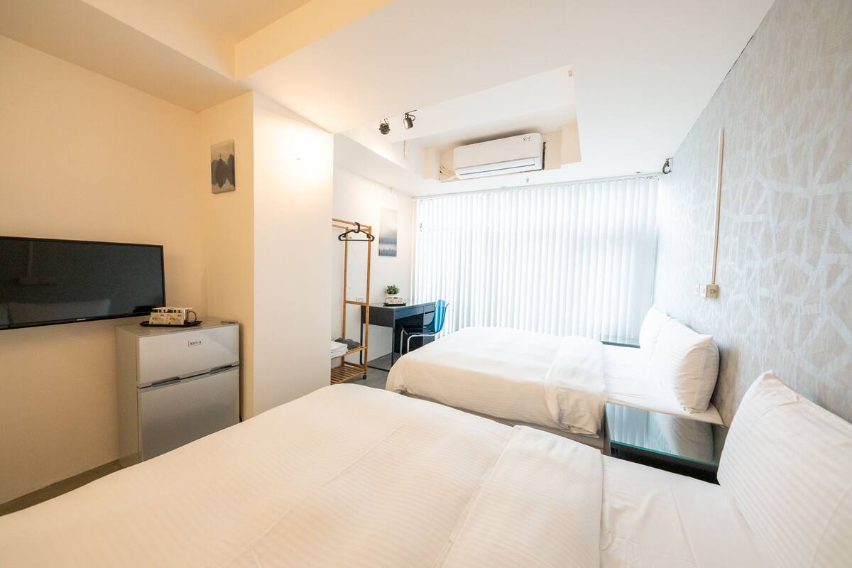 A hotel room with two beds, a desk, a chair, a TV, and a minibar.