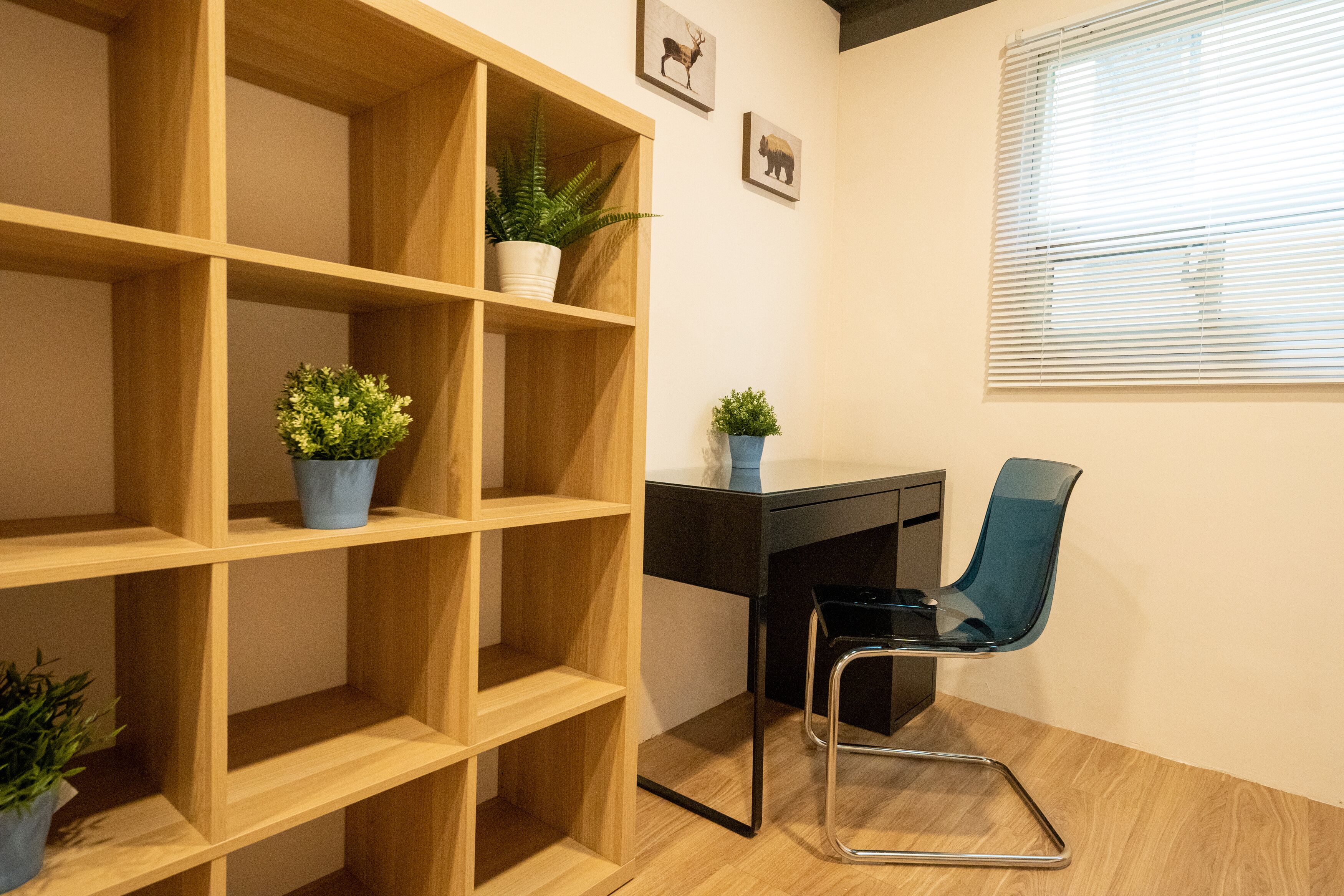 A room with a wooden shelving unit, a desk with a chair, and a window with blinds.