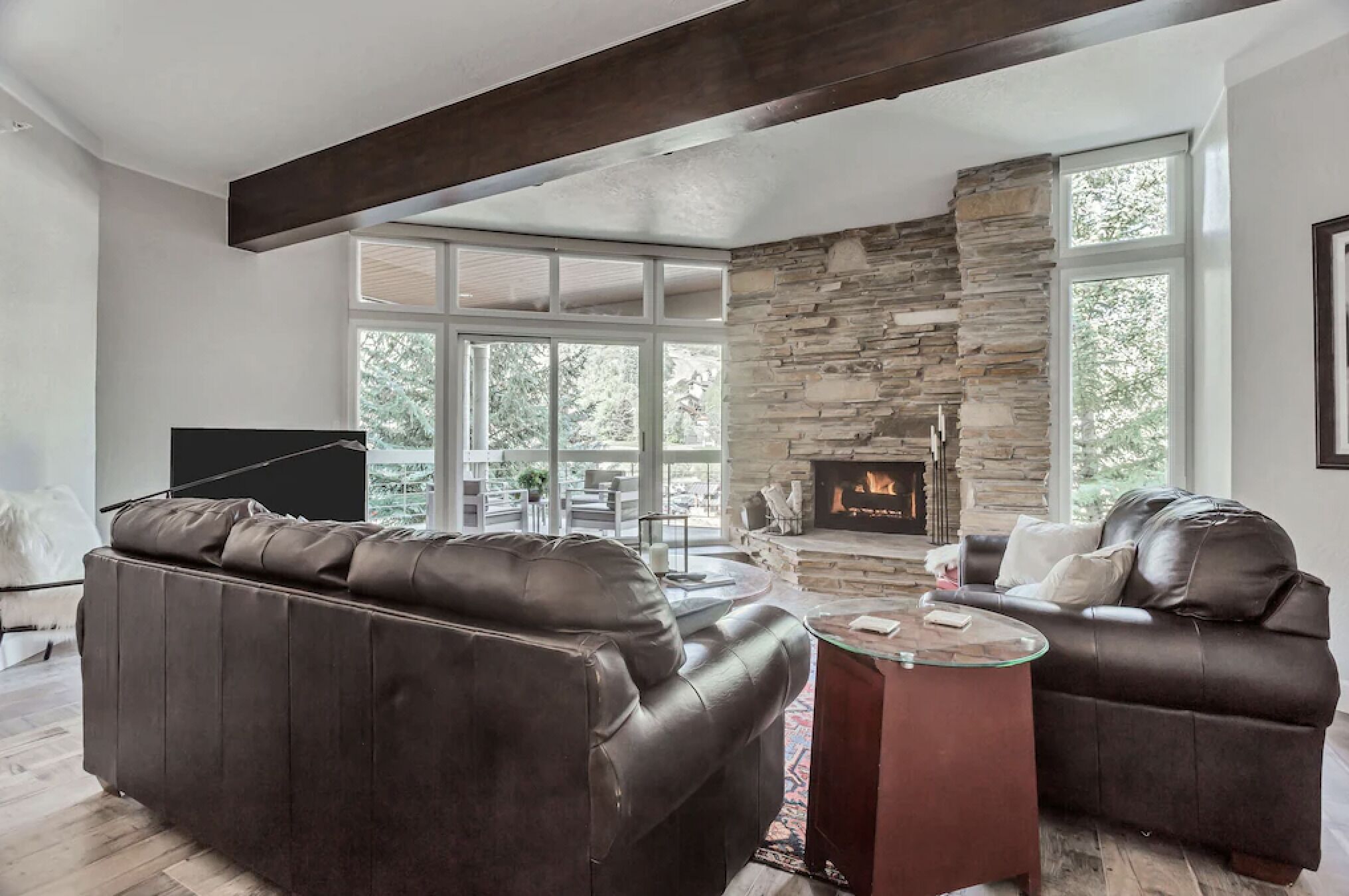 Una sala de estar moderna con chimenea de piedra, sofás de cuero y ventanas amplias.