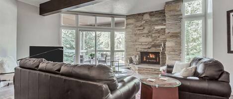 Una sala de estar moderna con chimenea de piedra, sofás de cuero y ventanas amplias.