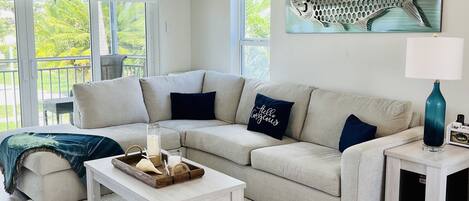 A modern living room with a sectional sofa, a coffee table, a lamp, and a ceiling fan.