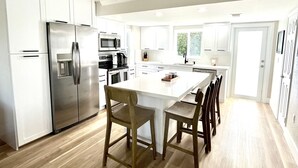 Une cuisine moderne avec des meubles blancs, des appareils en acier inoxydable et une table à manger en bois, assortie de chaises.