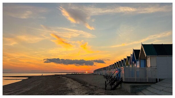Una playa con una hilera de tradicionales cabañas de madera, cielo despejado y una puesta de sol.