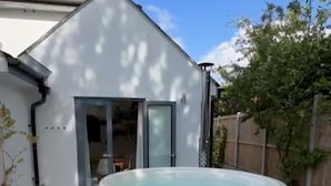 Un patio trasero con un jacuzzi, escalones que llevan a una puerta y un área cercada.