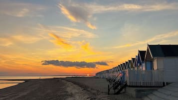 A beach with a row of traditional wooden beach huts, a clear sky, and a sunset.