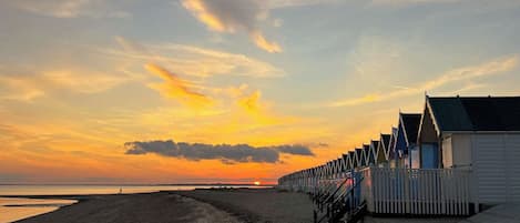 Una playa con una hilera de tradicionales cabañas de madera, cielo despejado y una puesta de sol.