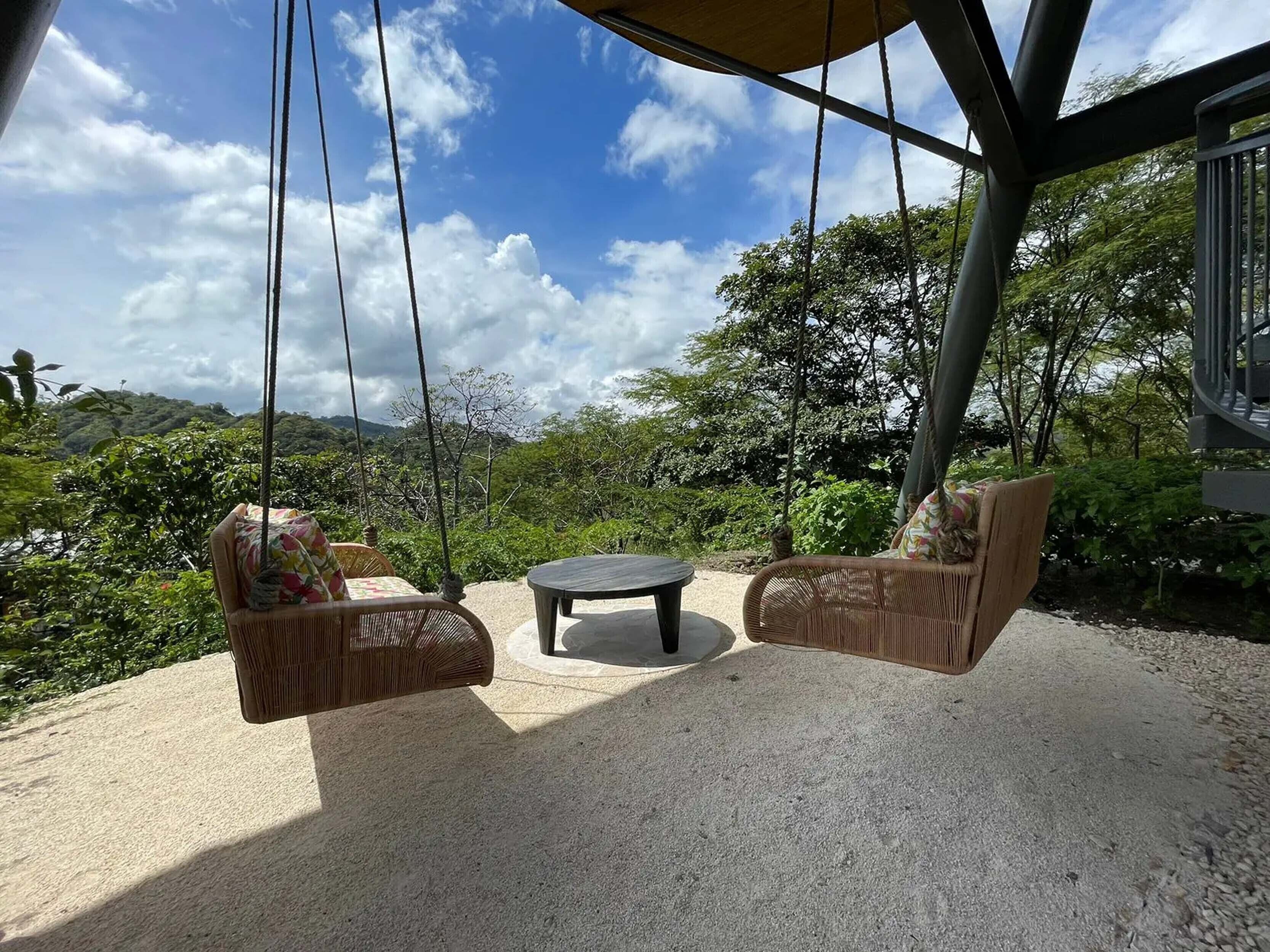 Eine Terrasse mit zwei Korbstühlen und einem kleinen runden Tisch, umgeben von Kiesböden und üppiger Bepflanzung.