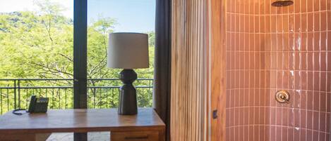 A room with a wooden desk, a lamp, and a view of greenery outside.