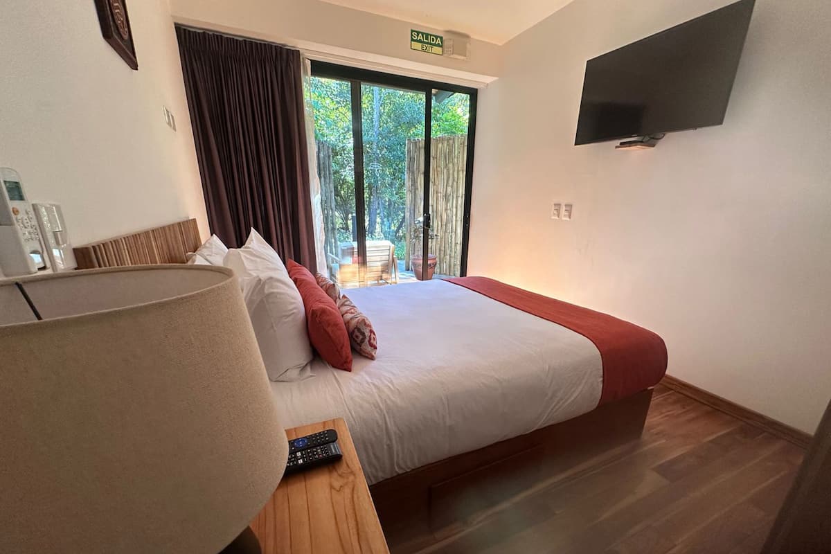 A hotel room with a large bed, a TV mounted on the wall, and a view of the outdoors through a sliding door.