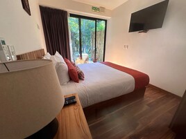 Quarto de hotel com uma cama grande, uma TV fixada na parede e vista para o exterior através de uma porta de correr.