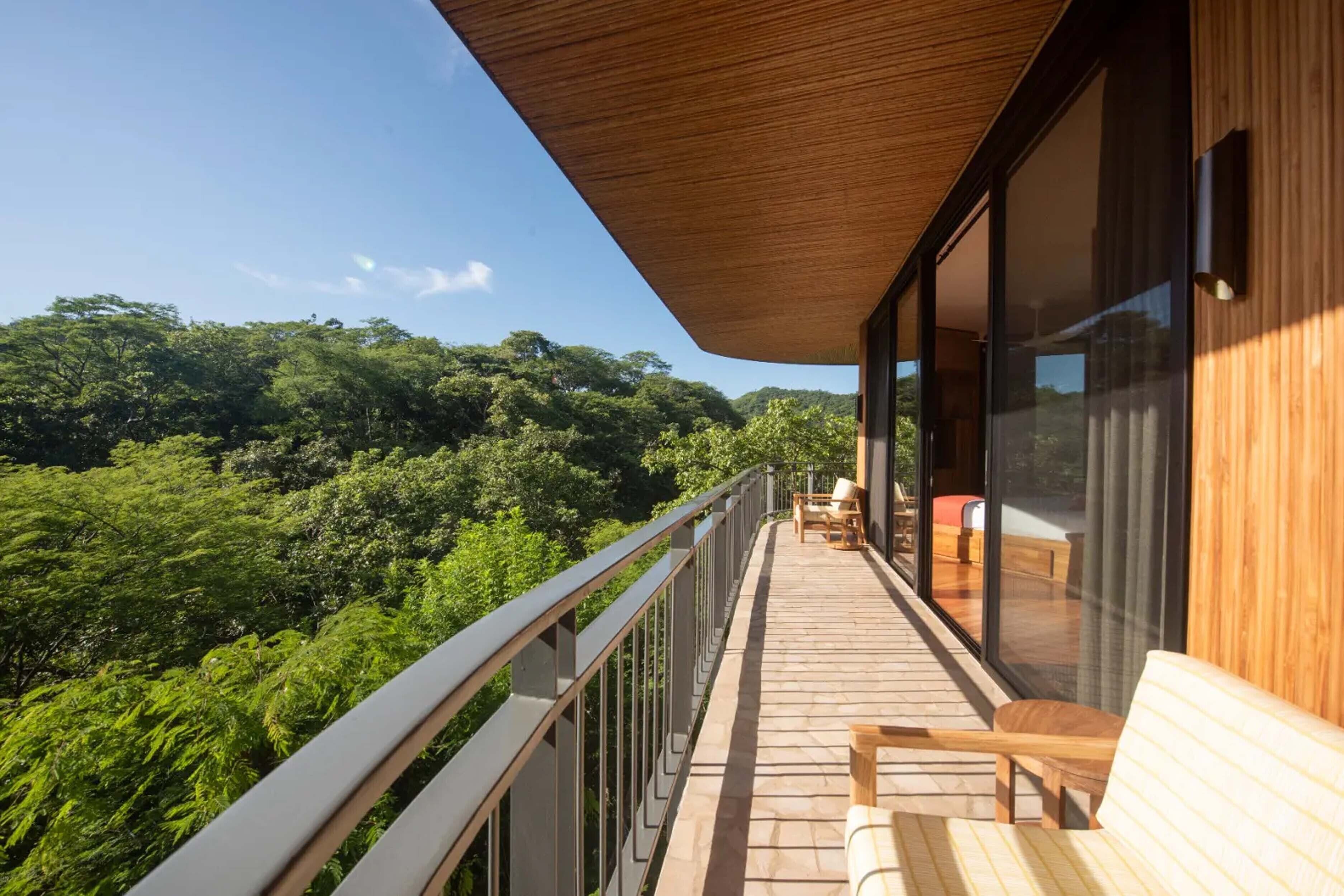 A balcony with wooden flooring, a metal railing, and a view of a lush forest.