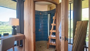 Una habitación con un escritorio de madera, una lámpara, zona de ducha con azulejos azules y una escalera de madera.