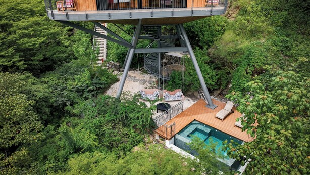 Una casa del árbol de gran altura con balcón, piscina y una escalera que conduce al nivel superior.