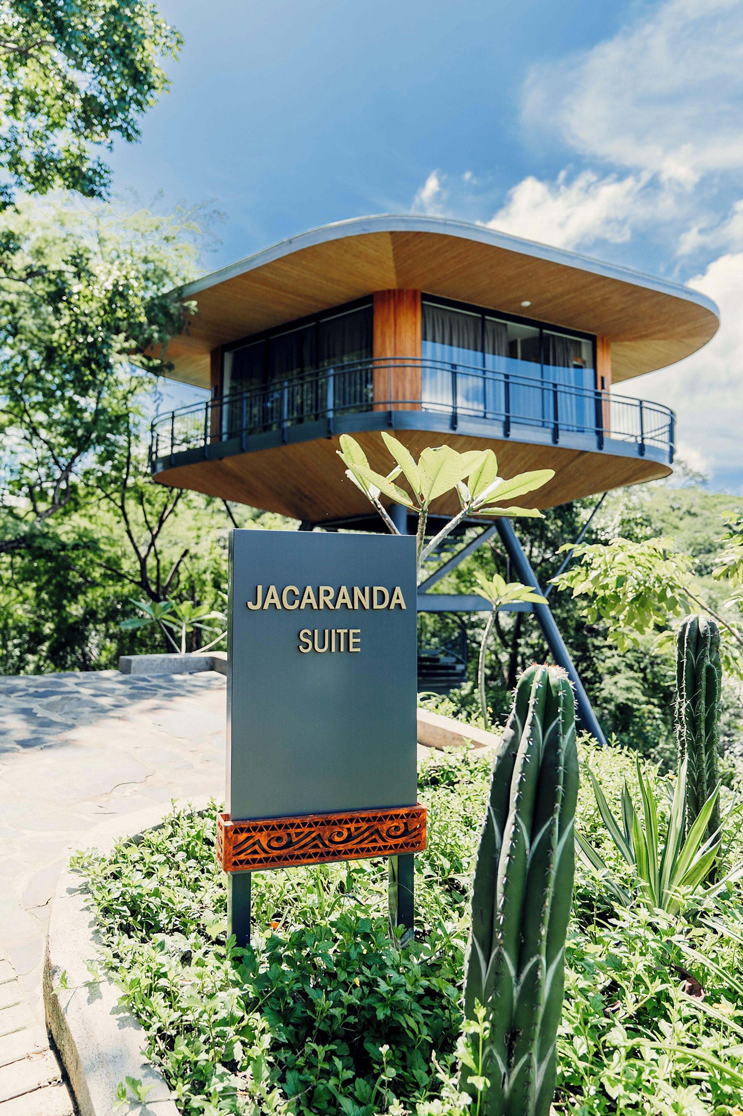 A sign for the Jacaranda Suite with a modern architectural design, surrounded by lush greenery and cacti.