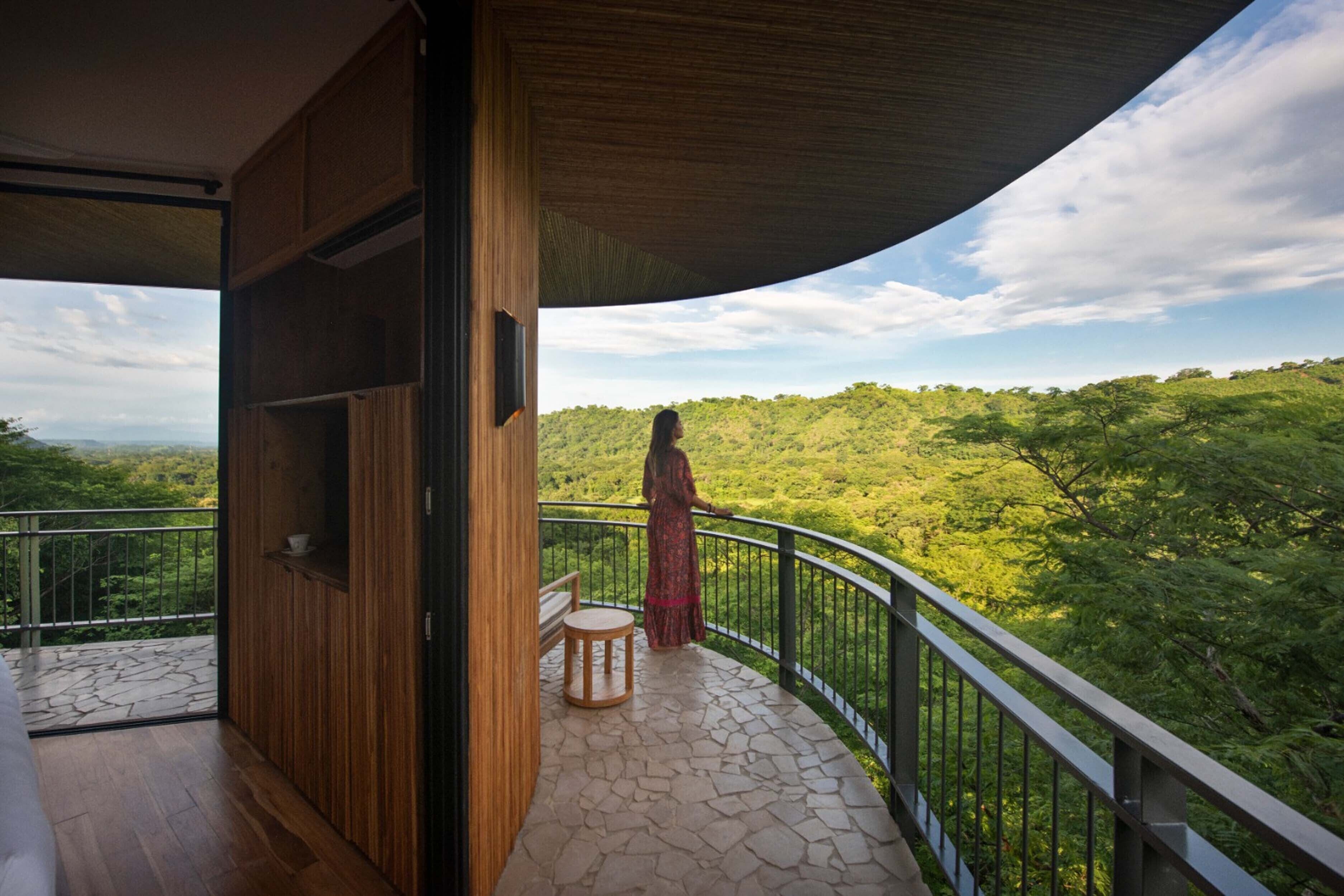 A balcony with a wooden floor and a stone-tiled floor, overlooking a lush green landscape.