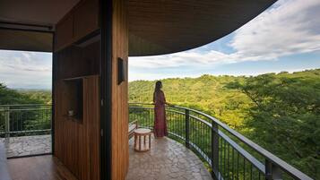 A balcony with a wooden floor and a stone-tiled floor, overlooking a lush green landscape.