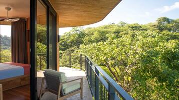 A balcony with a bed and a chair, overlooking a lush green forest.