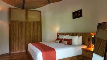 A neatly made bed with a red accent, wooden headboard, and a wall-mounted mirror.