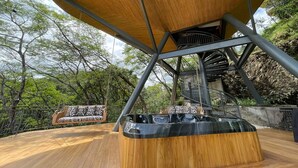 Una terraza de madera con una escalera espiral y un área de estar con cojines estampados.