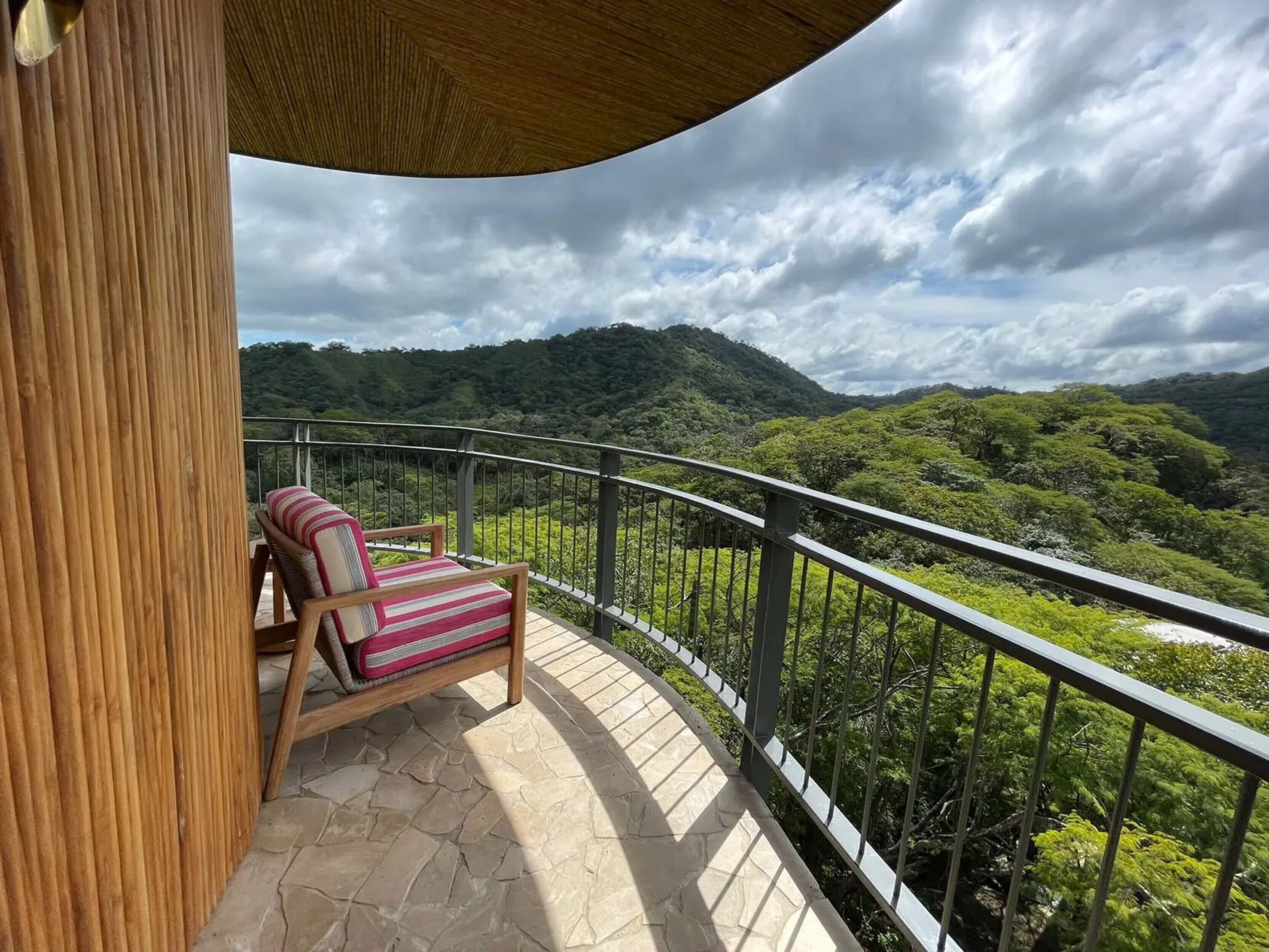 Un balcón con una silla de madera y vistas a un paisaje verde exuberante.