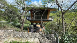 Una casa en árbol con una escalera de piedra que lleva a ella, rodeada de follaje.
